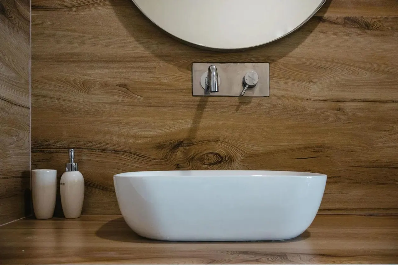 A bathroom vanity in figured timber with a round mirror and a white vessel basin