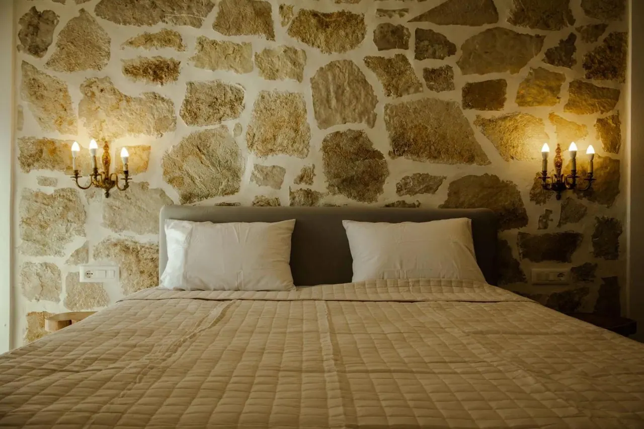 A double bed lit by two wall sconces against an exposed stone wall