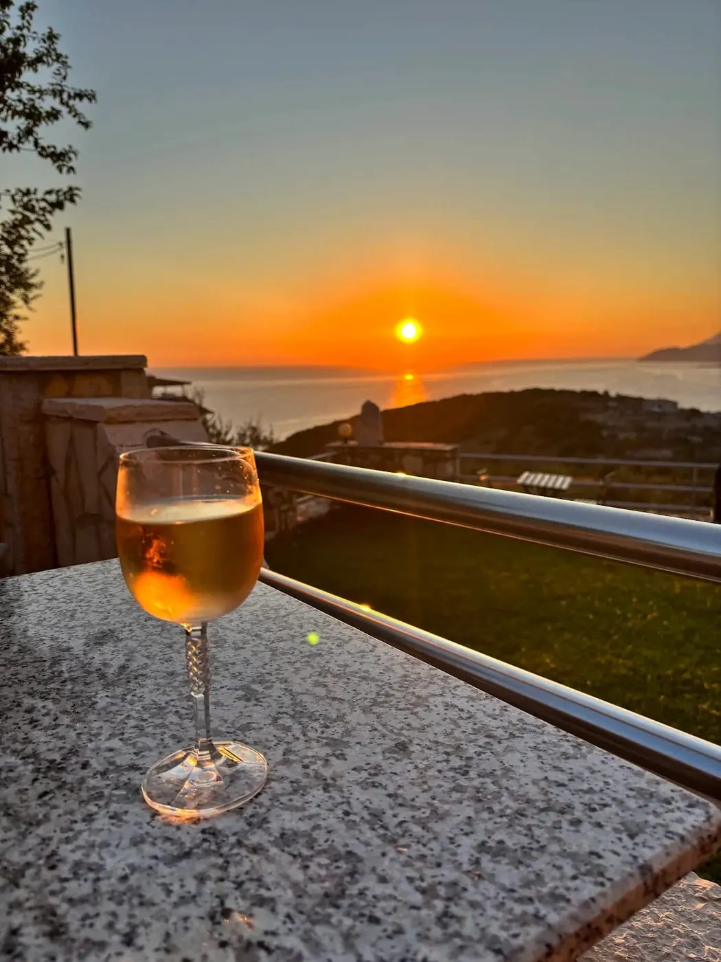 A glass of spritz on the terrace wall with the sun on the horizon behind it