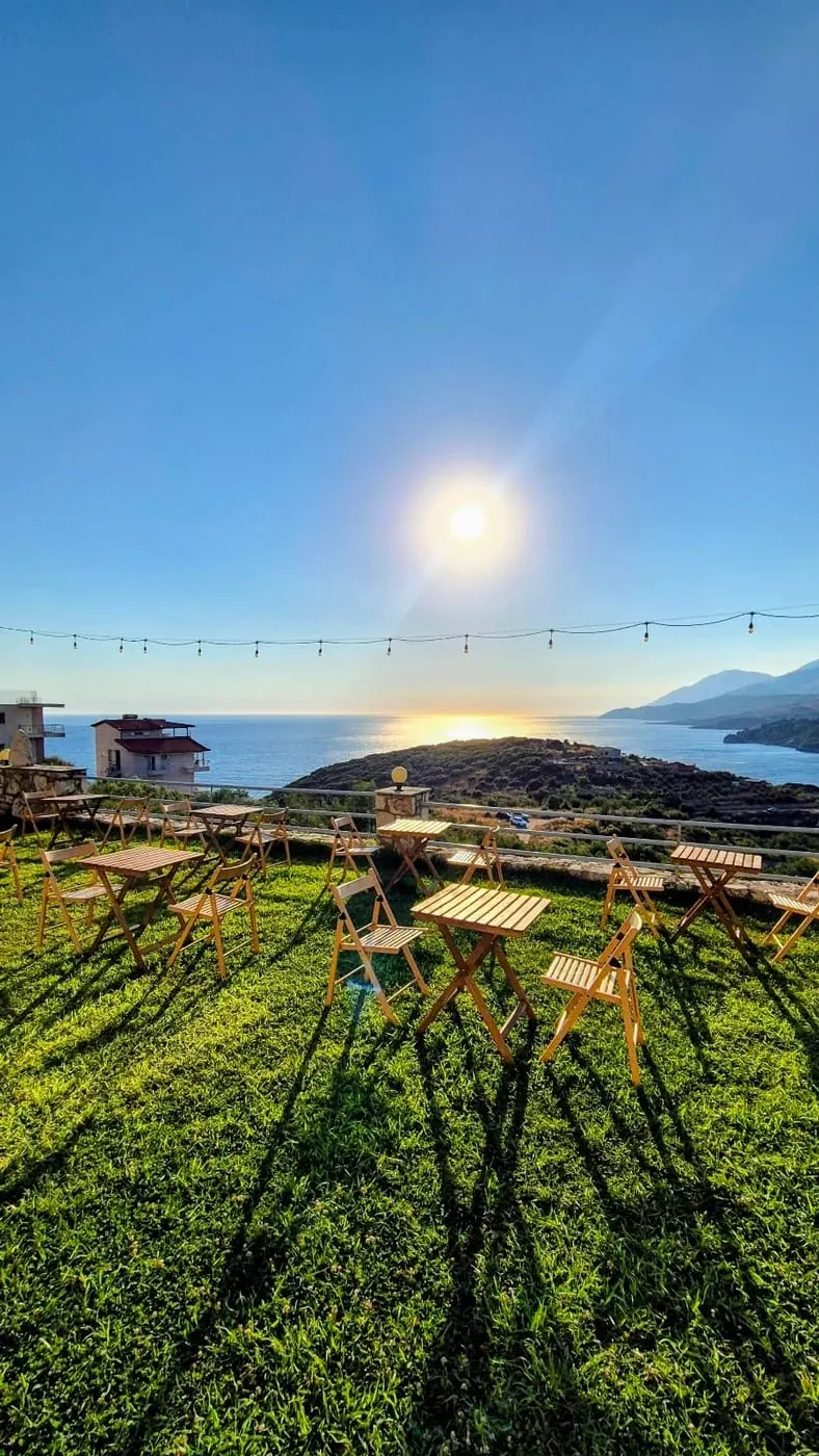 Empty folding wooden tables and chairs on a mown lawn with festoon lights and the bay beyond
