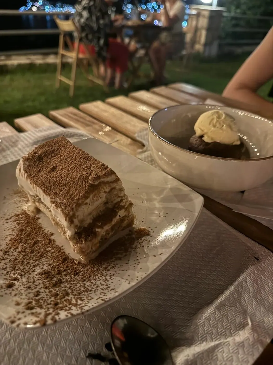A slice of tiramisu on a plate beside a bowl of ice cream