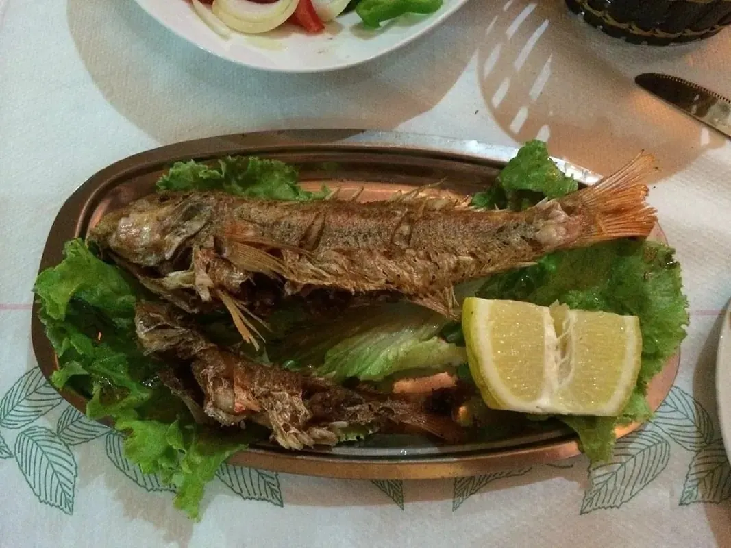 Two whole fried fish on a copper platter with lettuce and a wedge of lemon