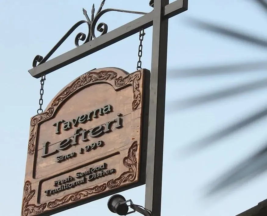Close view of the carved oak sign reading Taverna Lefteri, Since 1998, Fresh Seafood, Traditional Dishes