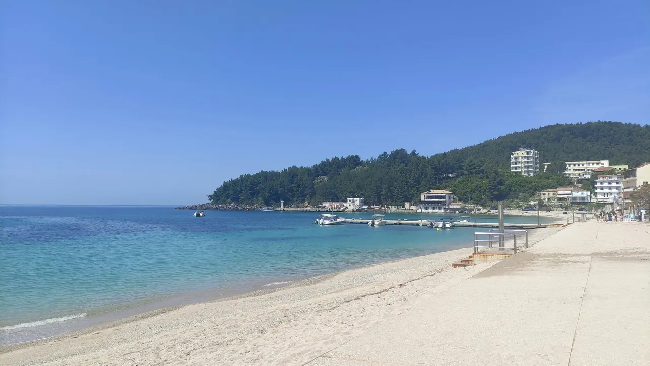 The pebble beach and pier at Spile, Himarë, with the pine-covered headland behind