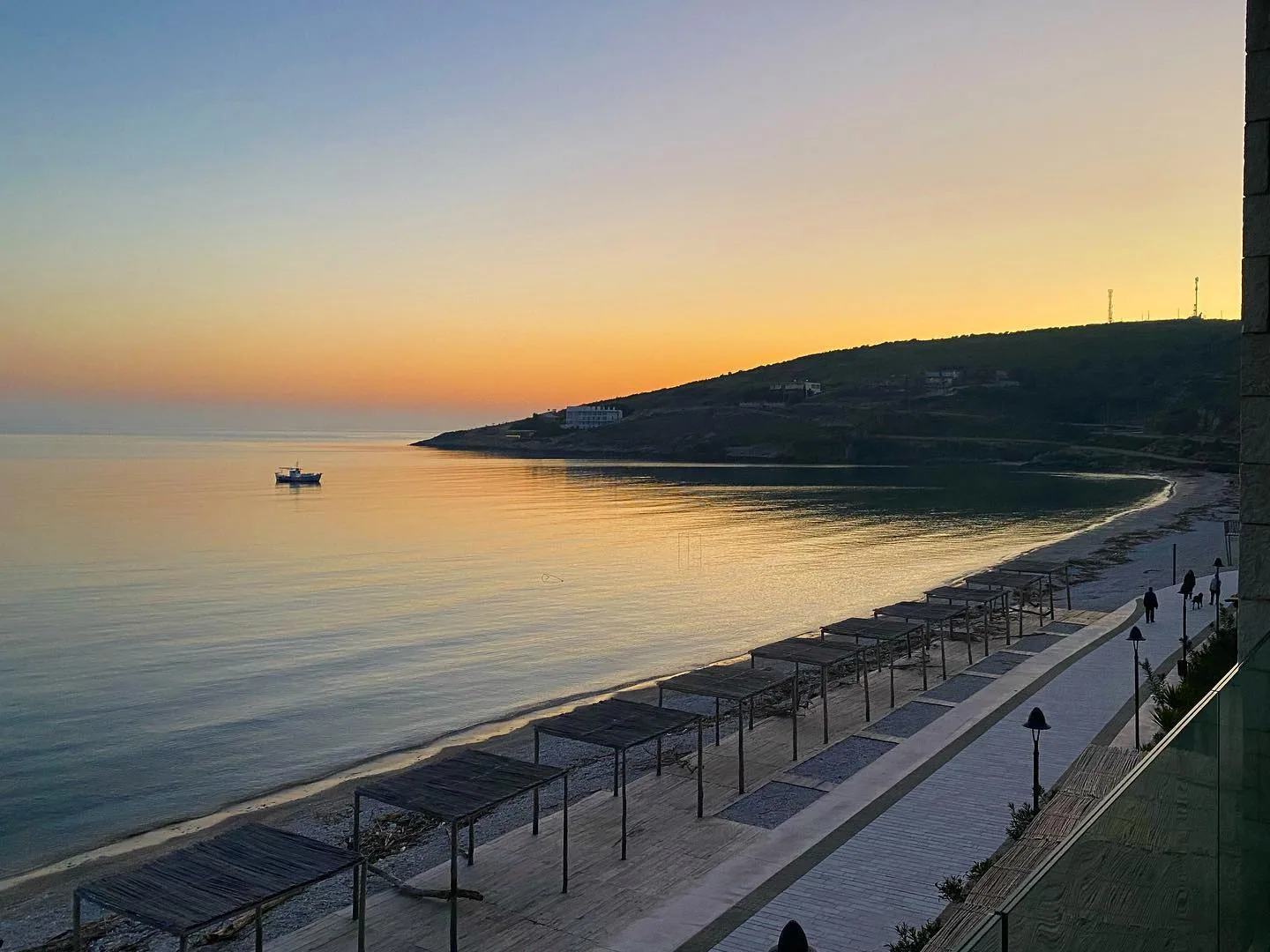 The Qeparo shore at dusk, the promenade lamps lit and the bay going flat and silver