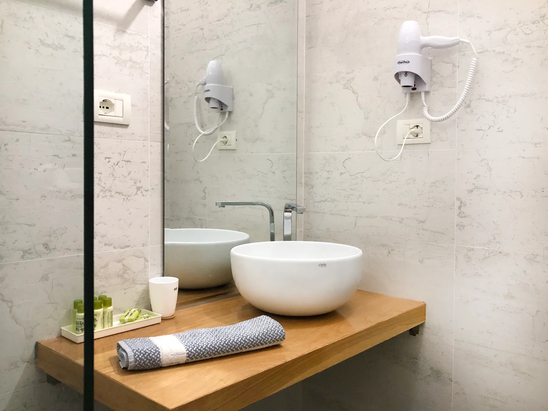 A walk-in shower and two bowl basins on a timber shelf in a marble bathroom