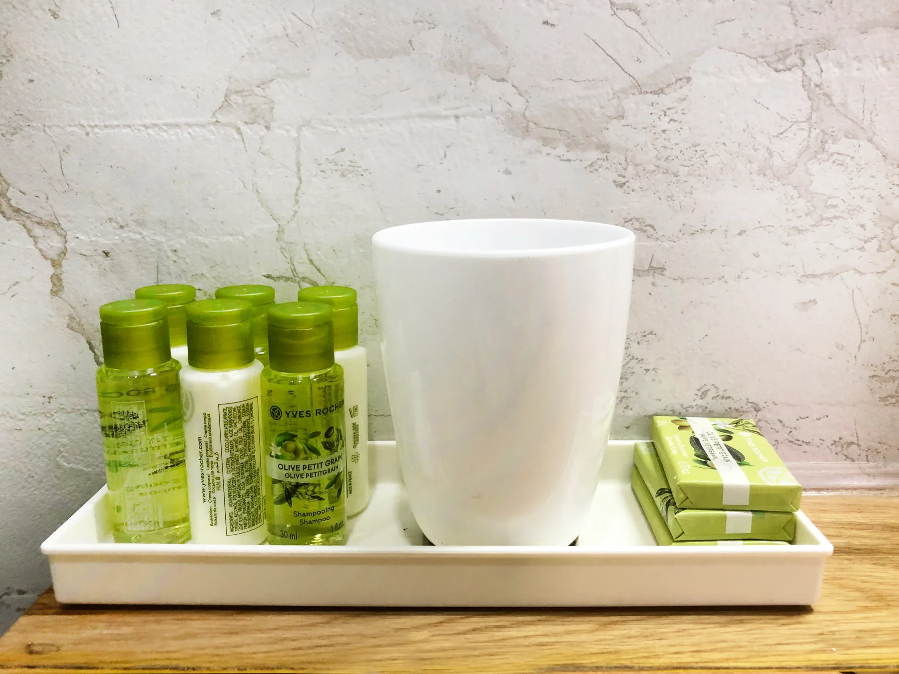 A tray of green toiletry bottles and wrapped soap beside a white cup
