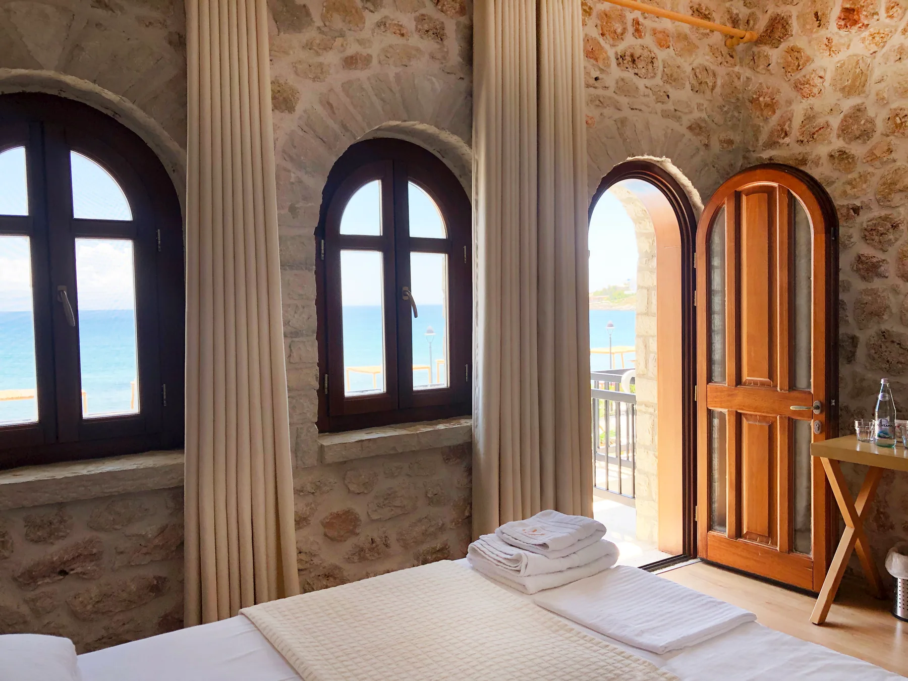 A double bed beside three arched windows and a timber arched door standing open to a balcony