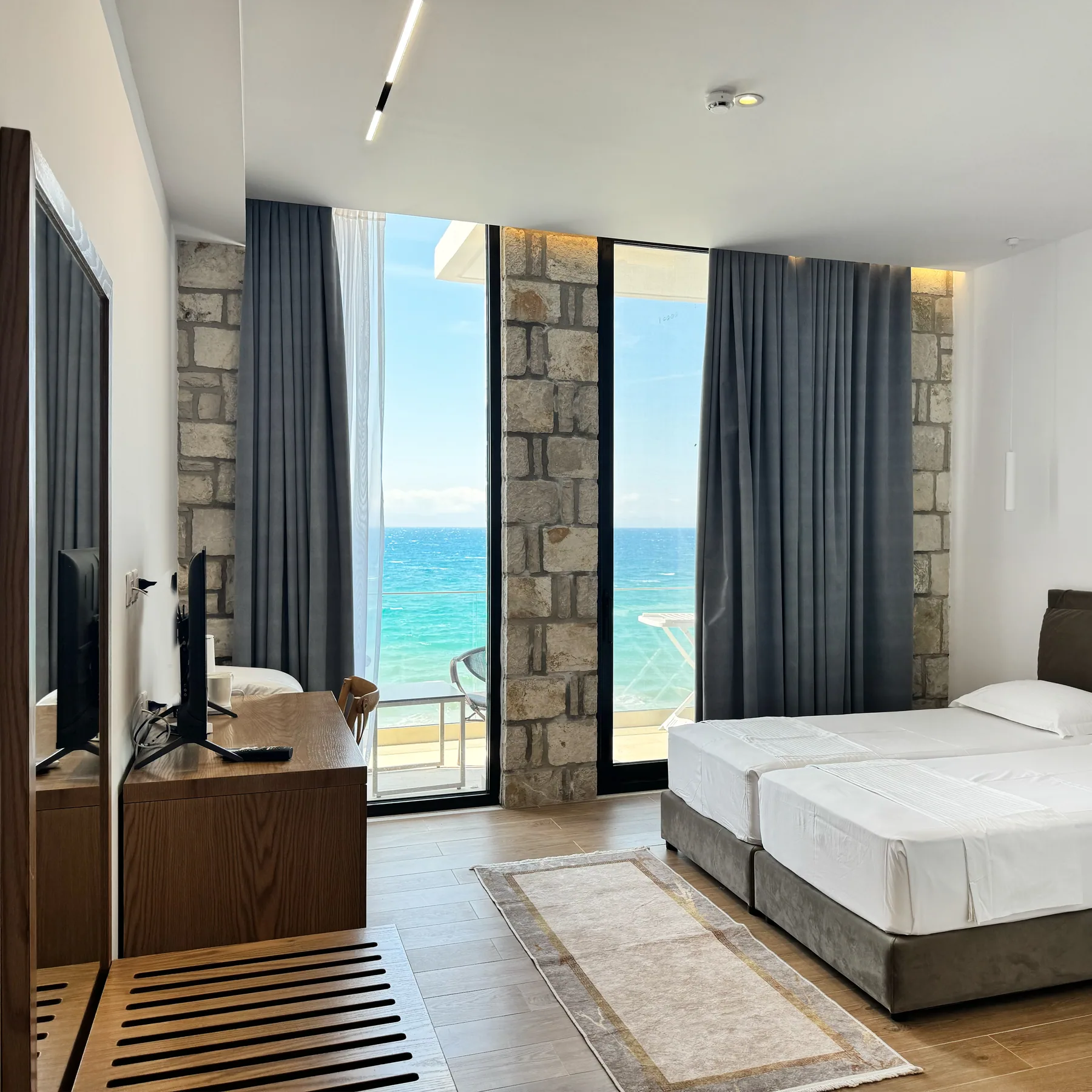 Twin beds and a television facing a wide window over the sea, a limestone pier at the corner