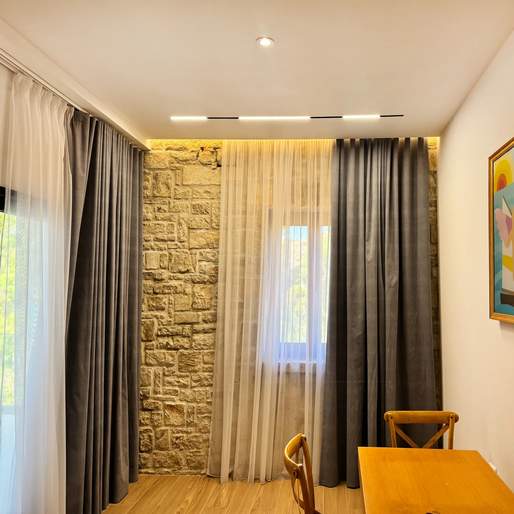 A made bed against a limestone accent wall with cream curtains either side