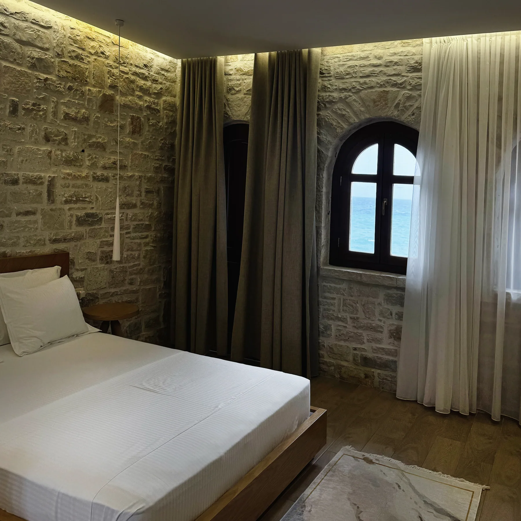 A bed in a stone-walled room lit by a small arched window