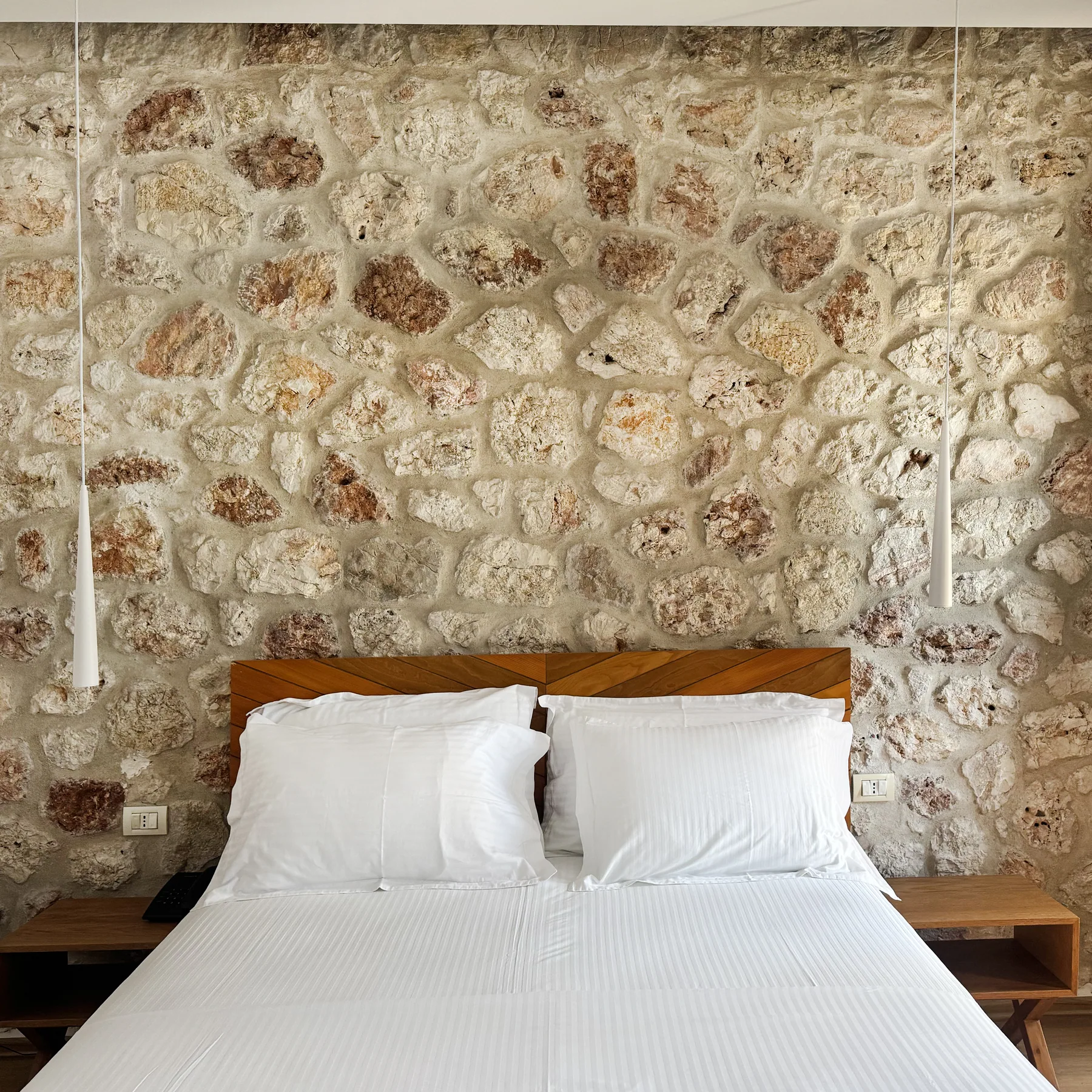 A double bed with a timber chevron headboard against rough limestone