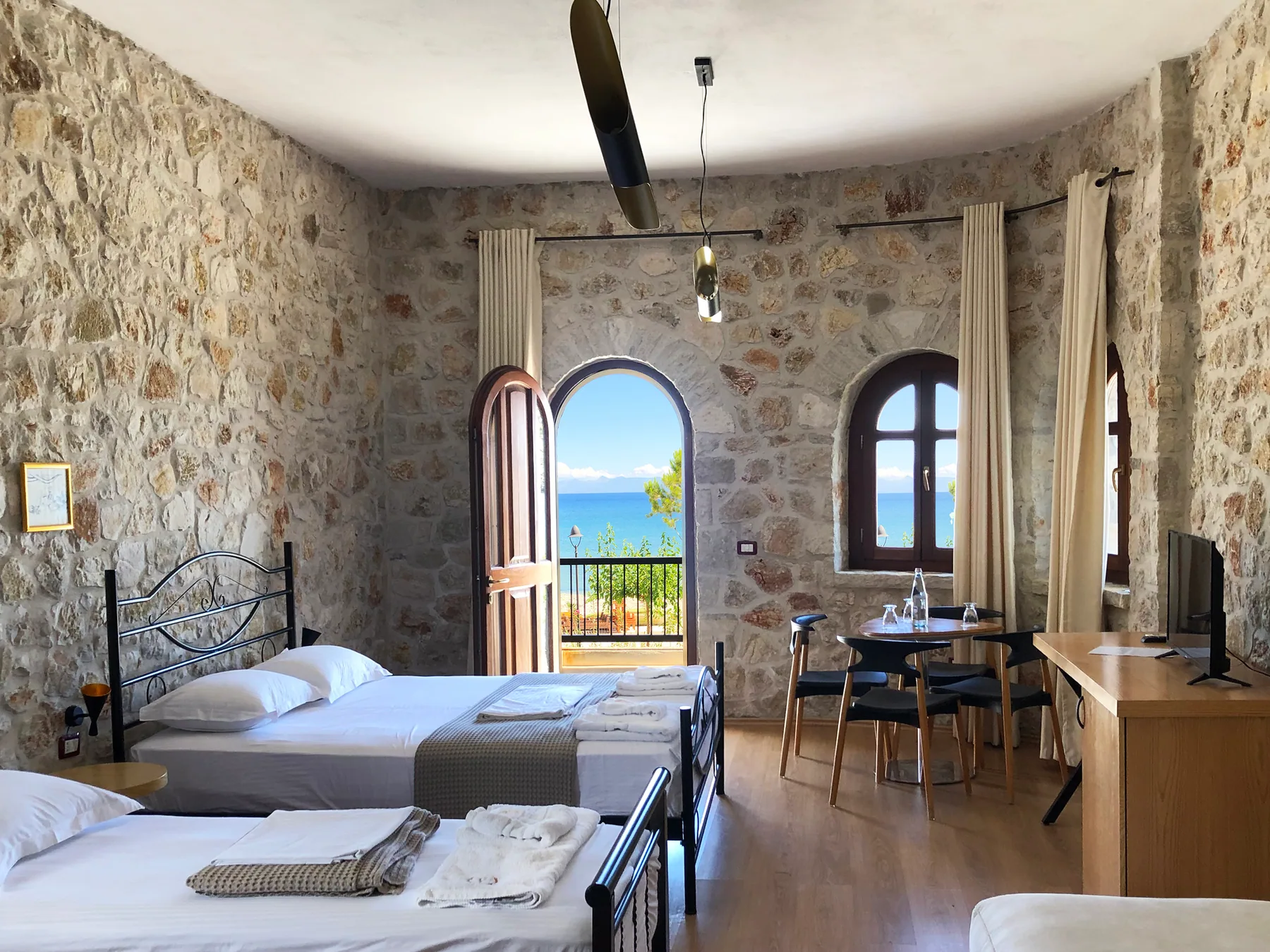 A stone-walled room with an arched window over the sea, a round table and four chairs