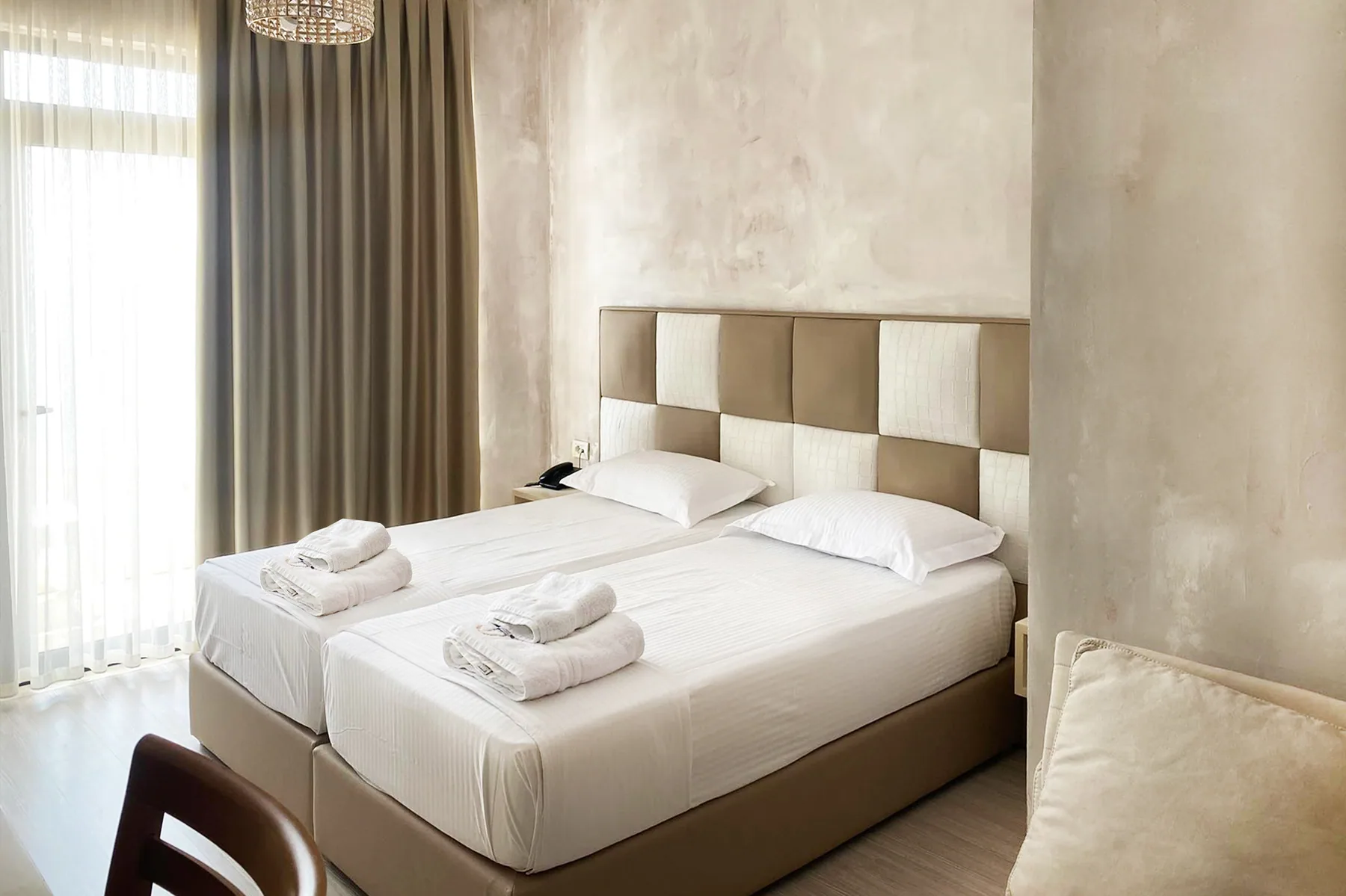 Twin beds with a checkered upholstered headboard in a pale plaster room