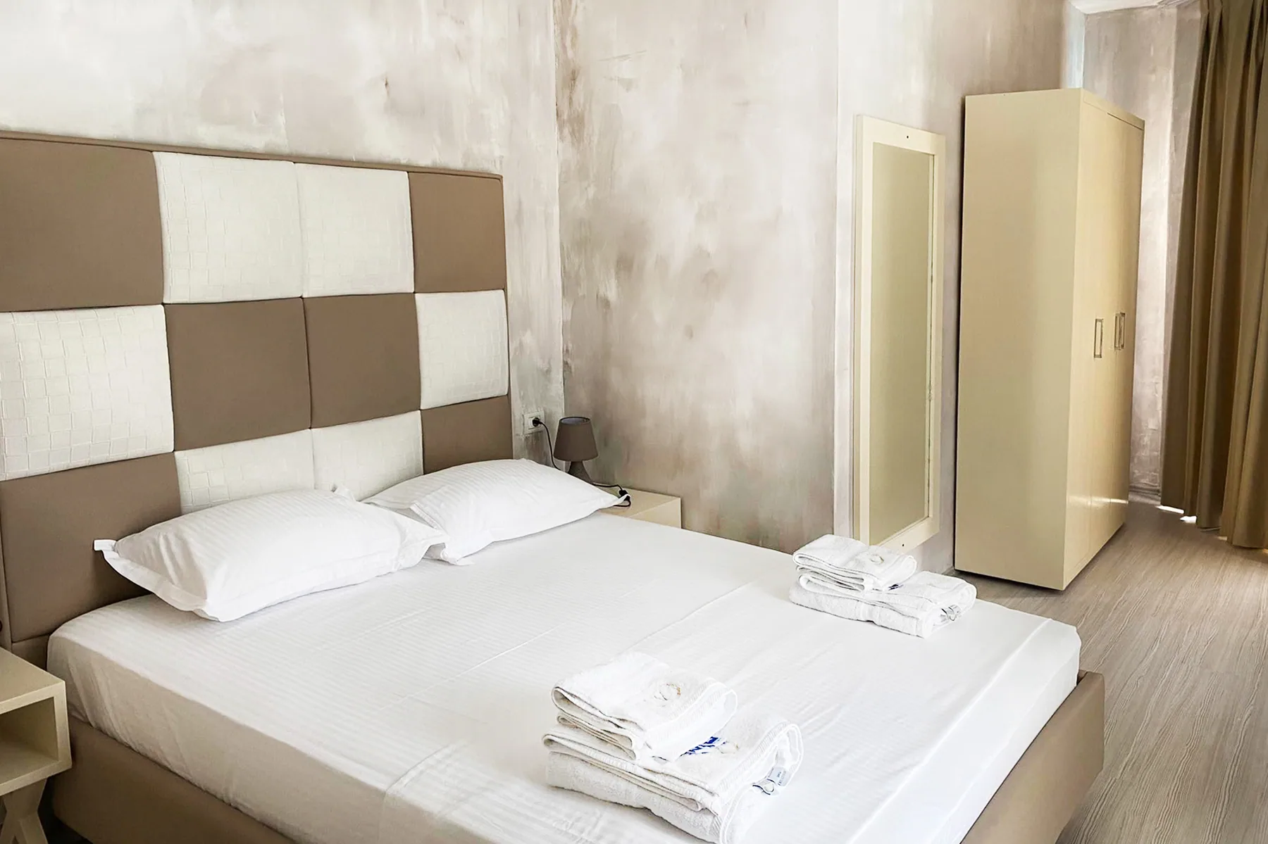 A wide bed under a checkered headboard beside a fitted wardrobe in pale plaster