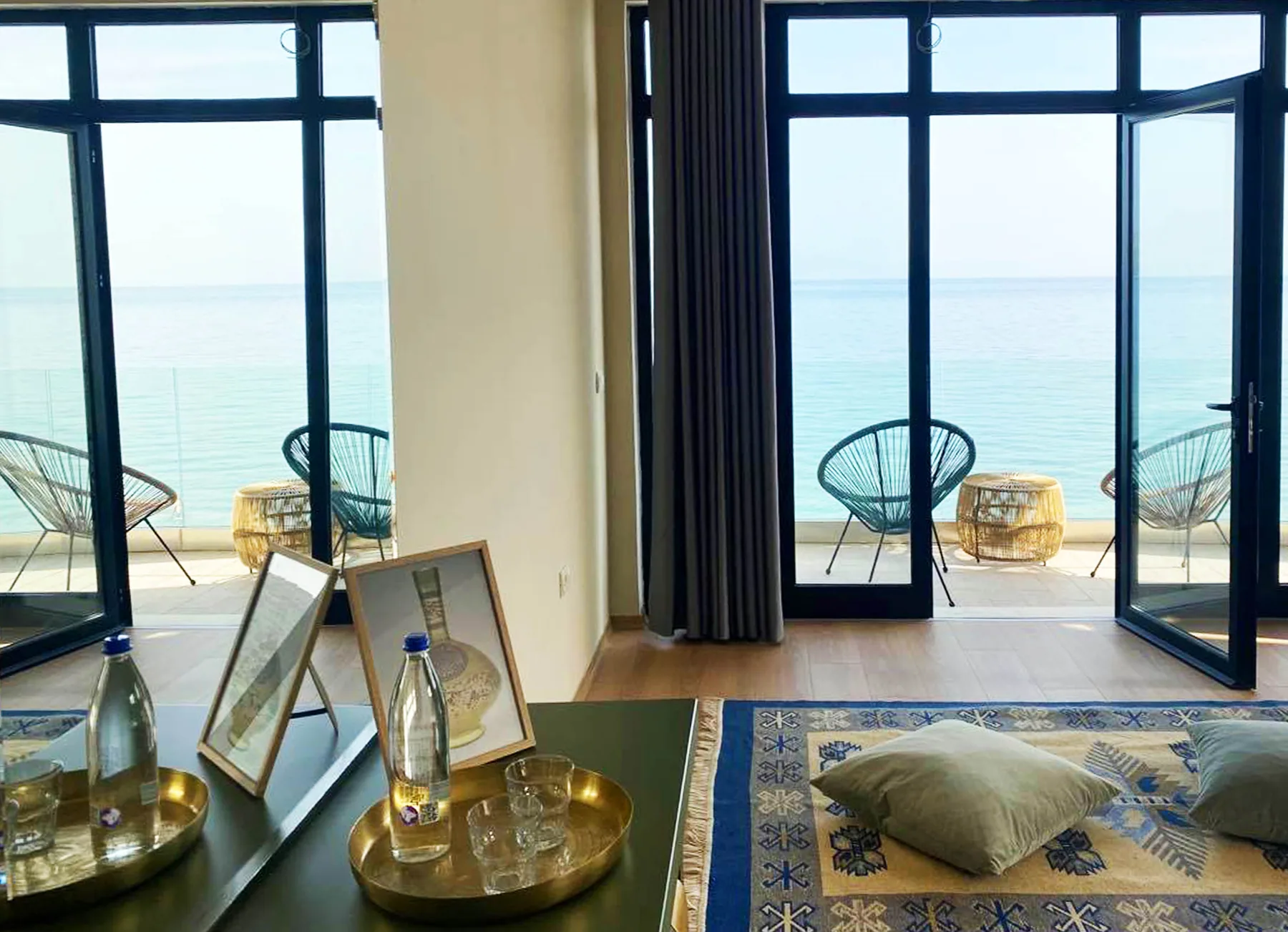 Black-framed glazed doors standing open onto a terrace at beach level with the sea beyond