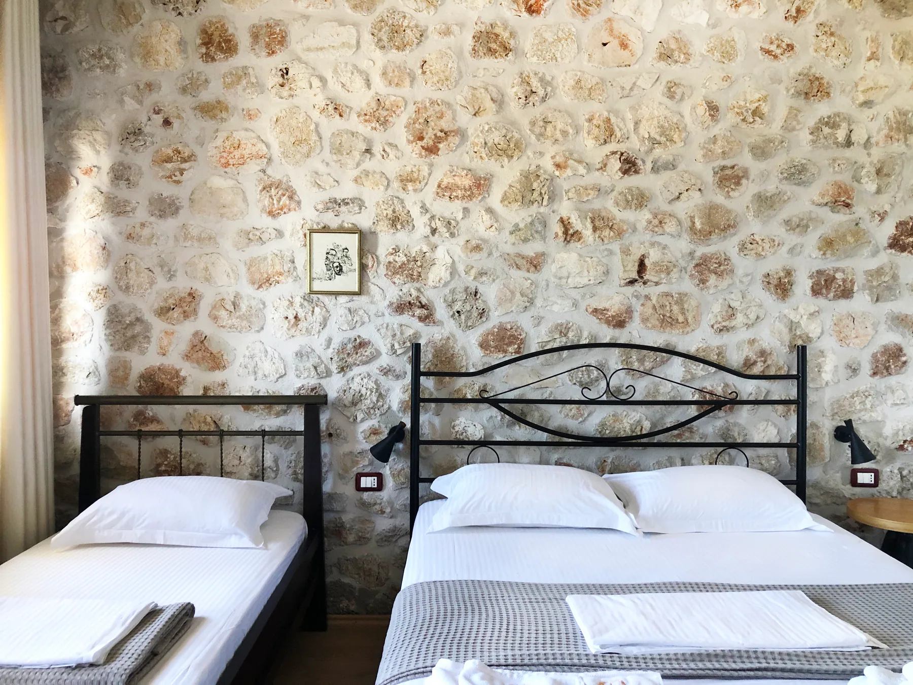 A single bed and a double bed with wrought-iron headboards against a limestone wall