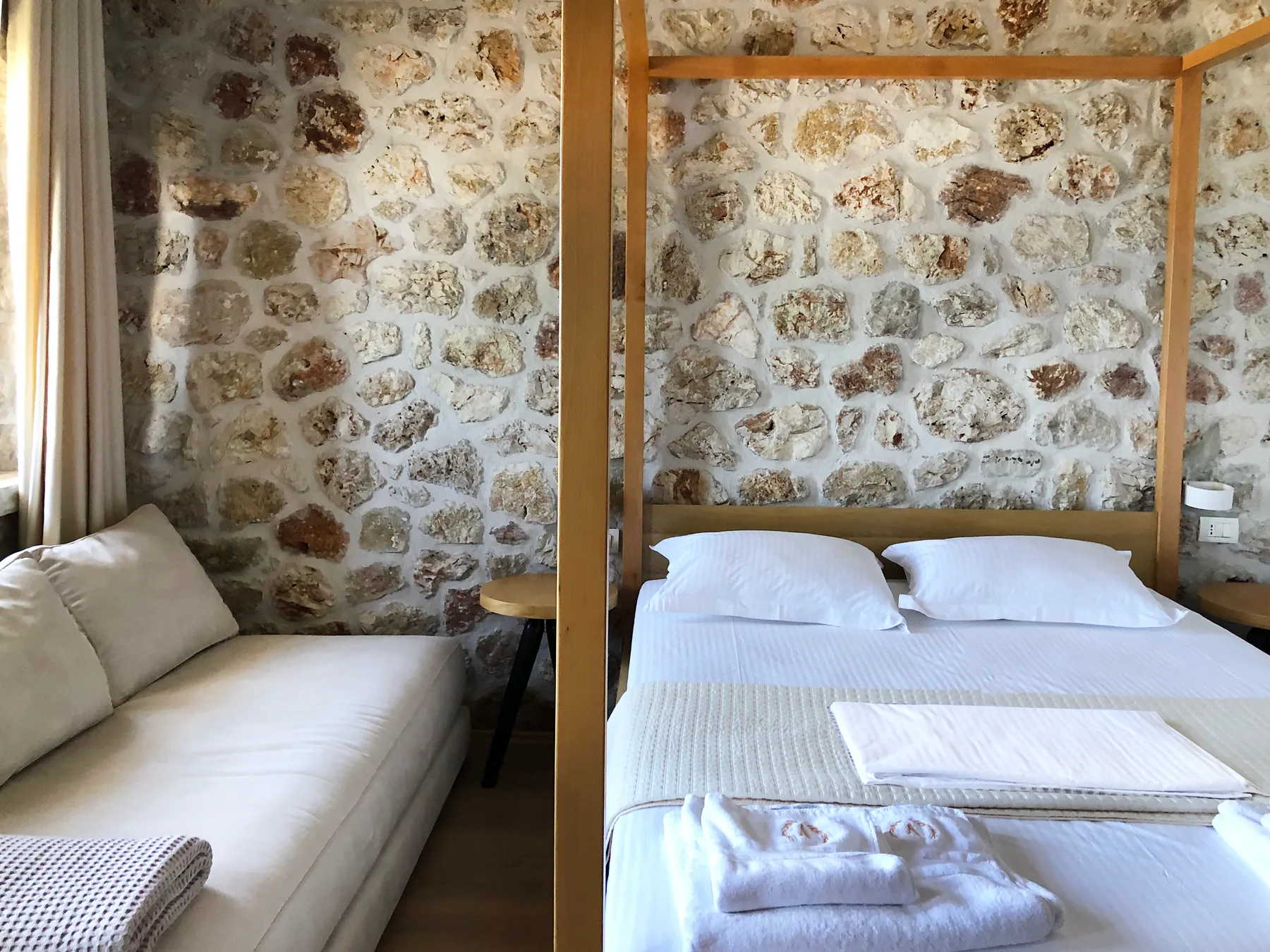 A sofa bed beside a double bed under a timber four-poster frame in a stone-walled room