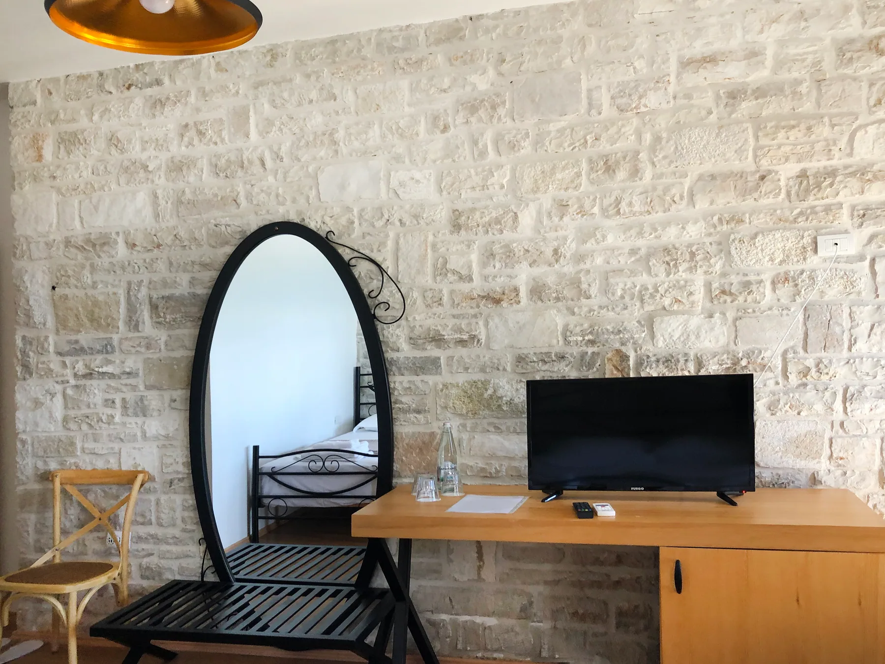 An oval mirror, a writing desk and a television on a limestone wall beside a folding chair