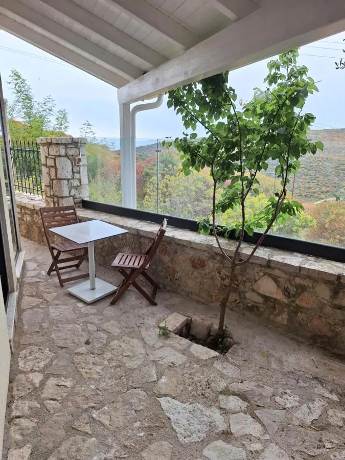 A covered stone terrace with a small table and two folding chairs, looking out over the hillside
