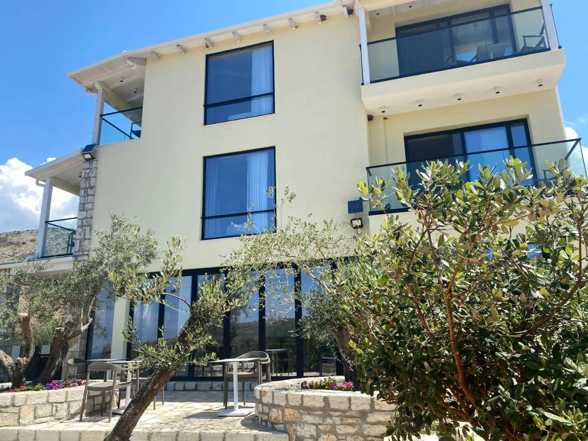 The cream-rendered building from the garden, three storeys of glass balconies above a glazed ground floor, olive trees in front