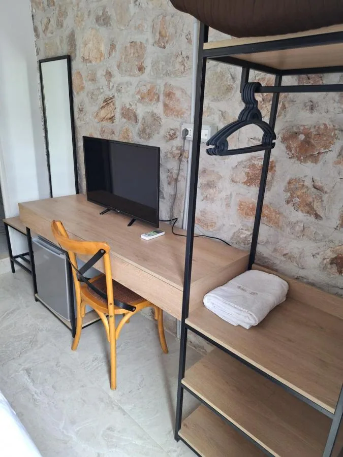 A timber desk and open clothes rail against the exposed stone wall, a folded towel embroidered Vila D