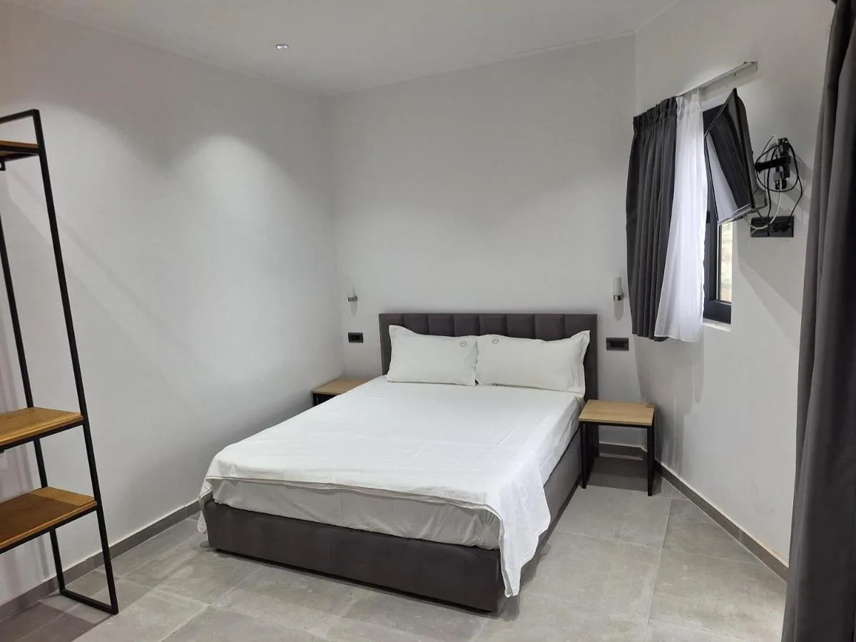 A plain double room in white with an upholstered headboard and a wall-mounted television