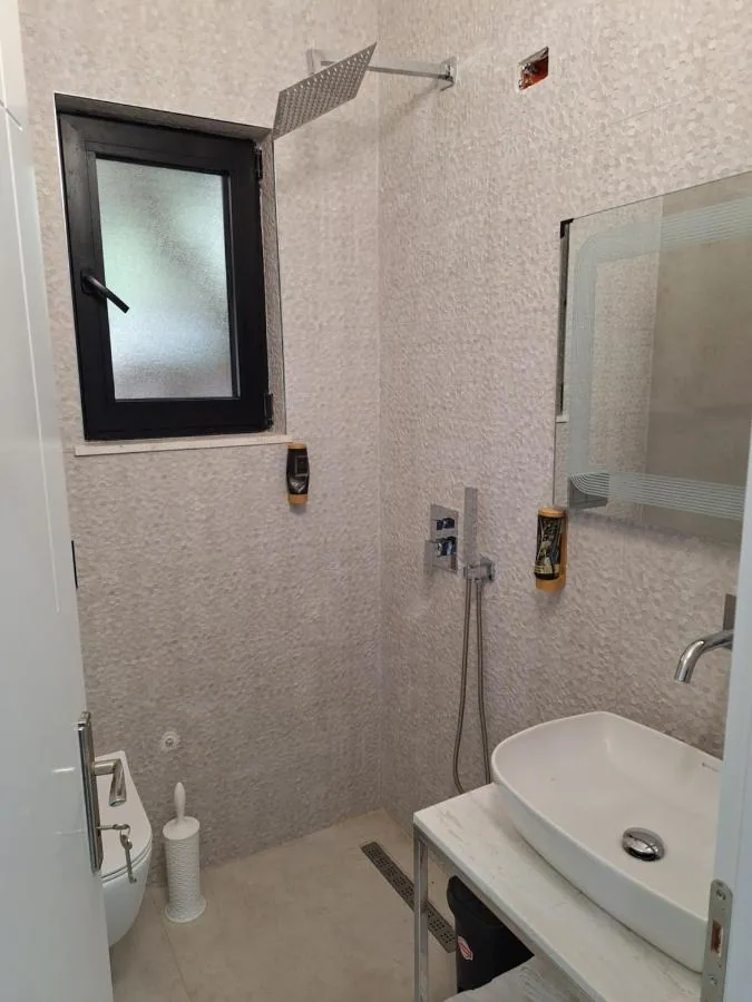 A rain shower head over a stone-tiled wet room beside a basin
