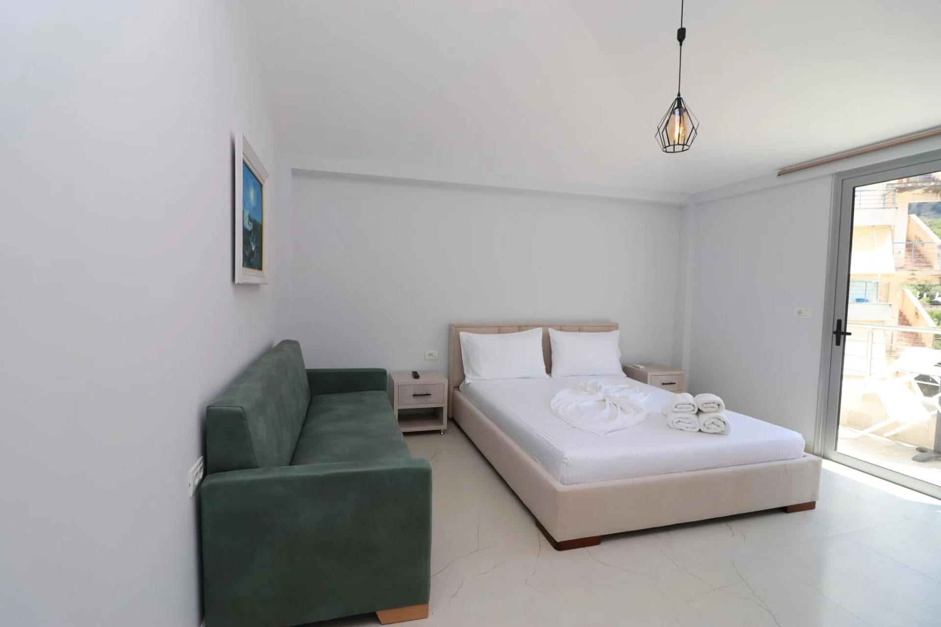Bedroom with a wide bed, a green sofa and a sliding door onto the balcony