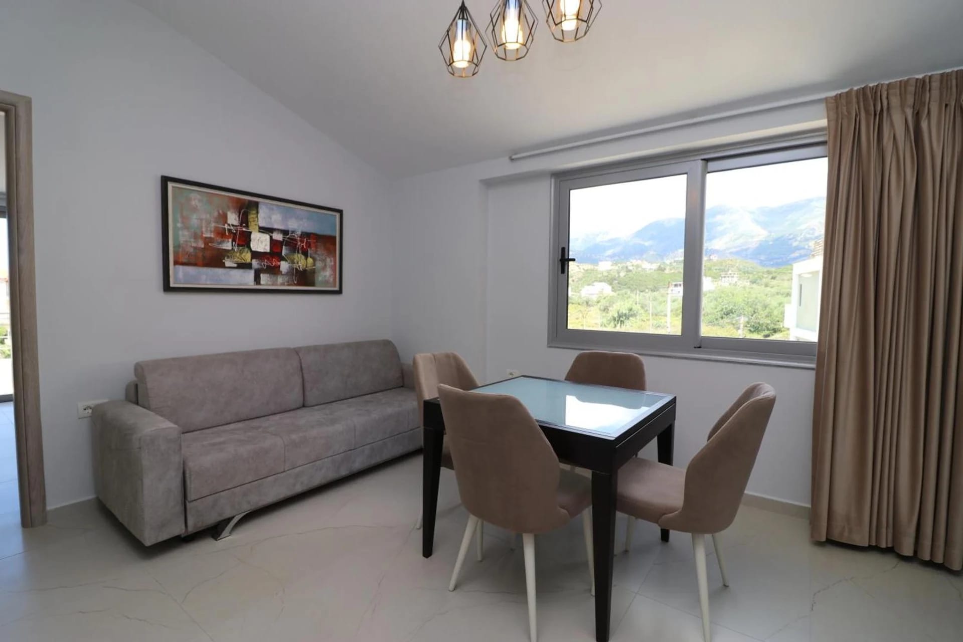 Apartment living room with a sofa, dining table and a window onto the mountains
