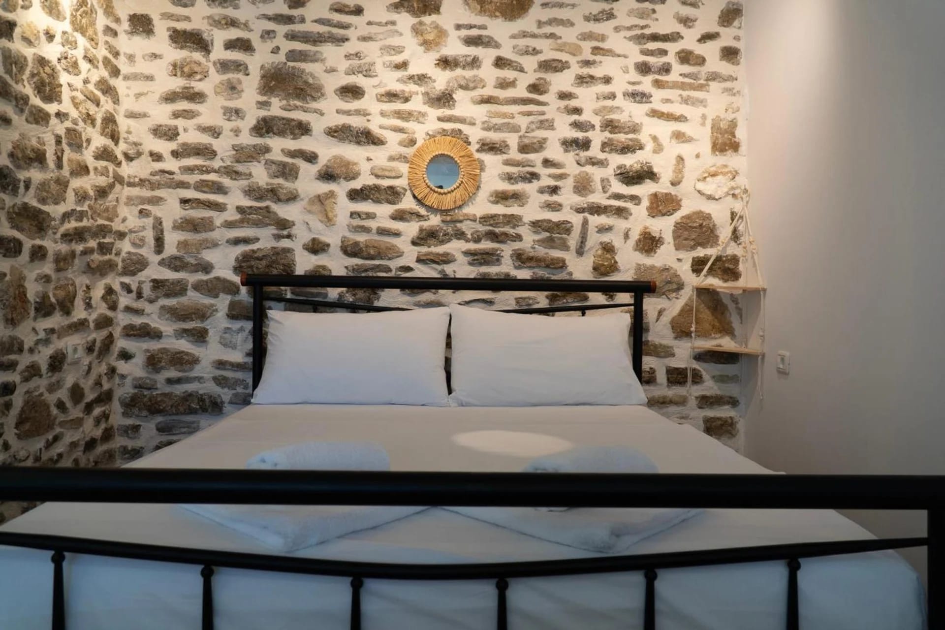 Double room with a black iron bed against an exposed stone wall