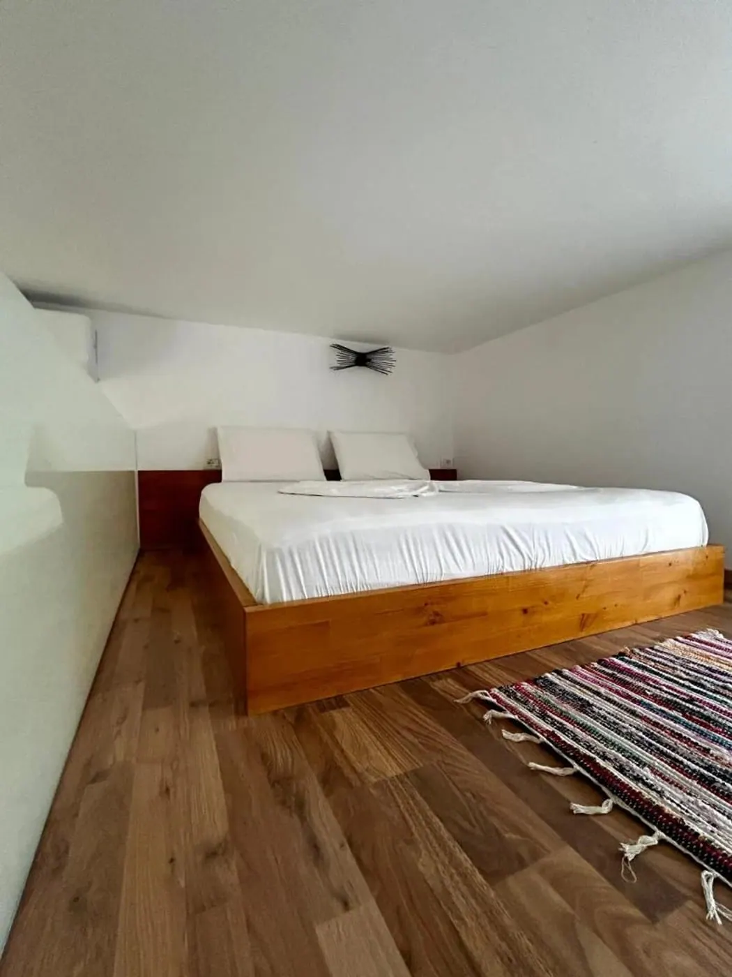 Bed on a walnut floor with a woven kilim runner alongside