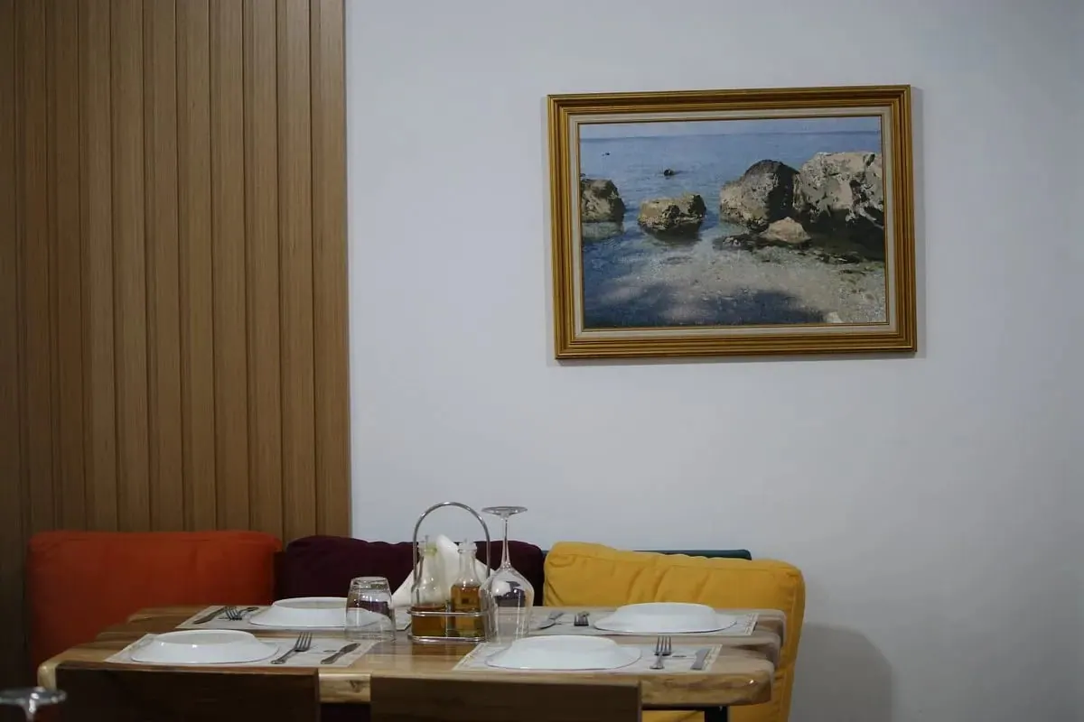 A corner table for three against a timber-slatted wall, with a gold-framed seascape above the banquette