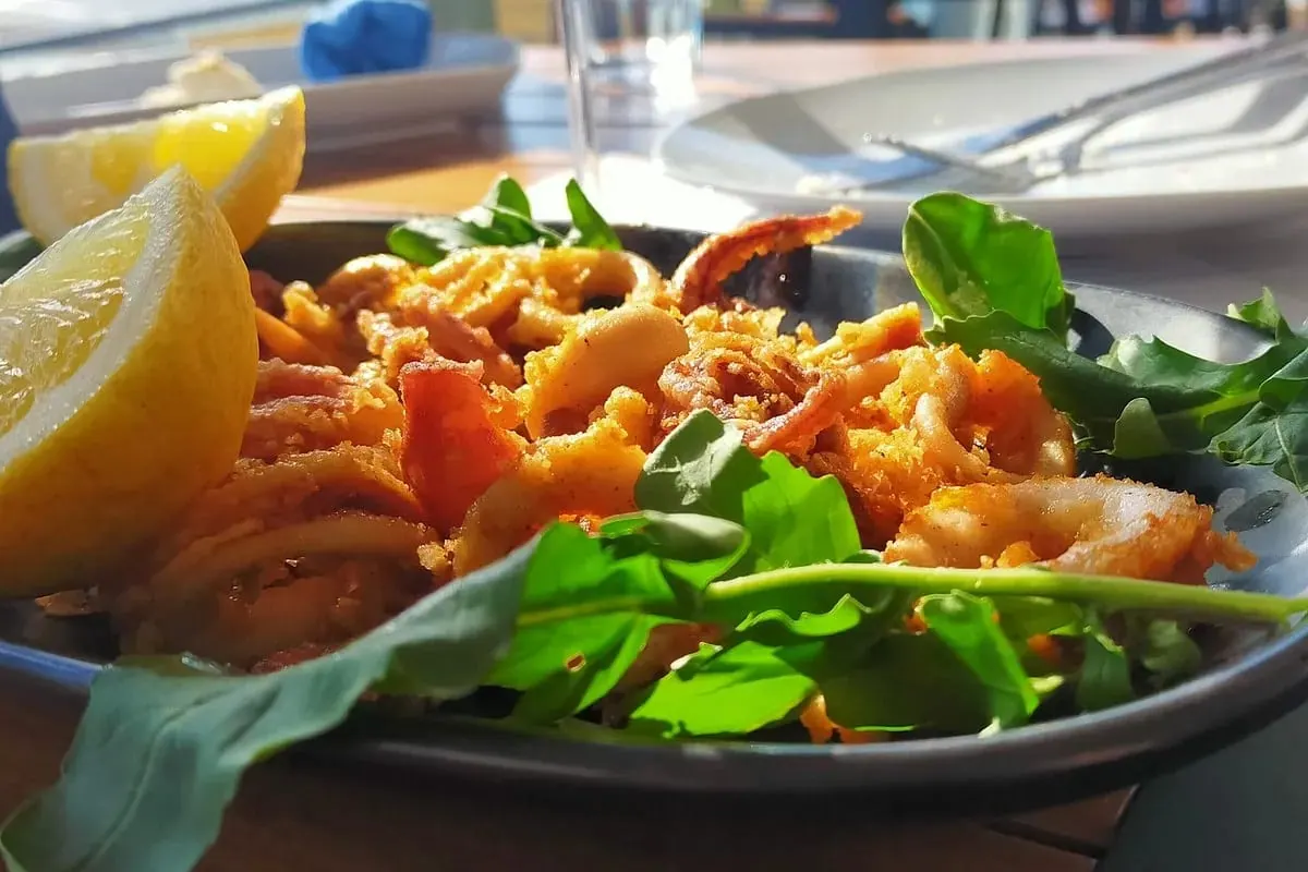Golden fried calamari and rocket leaves in a dark bowl with two lemon wedges