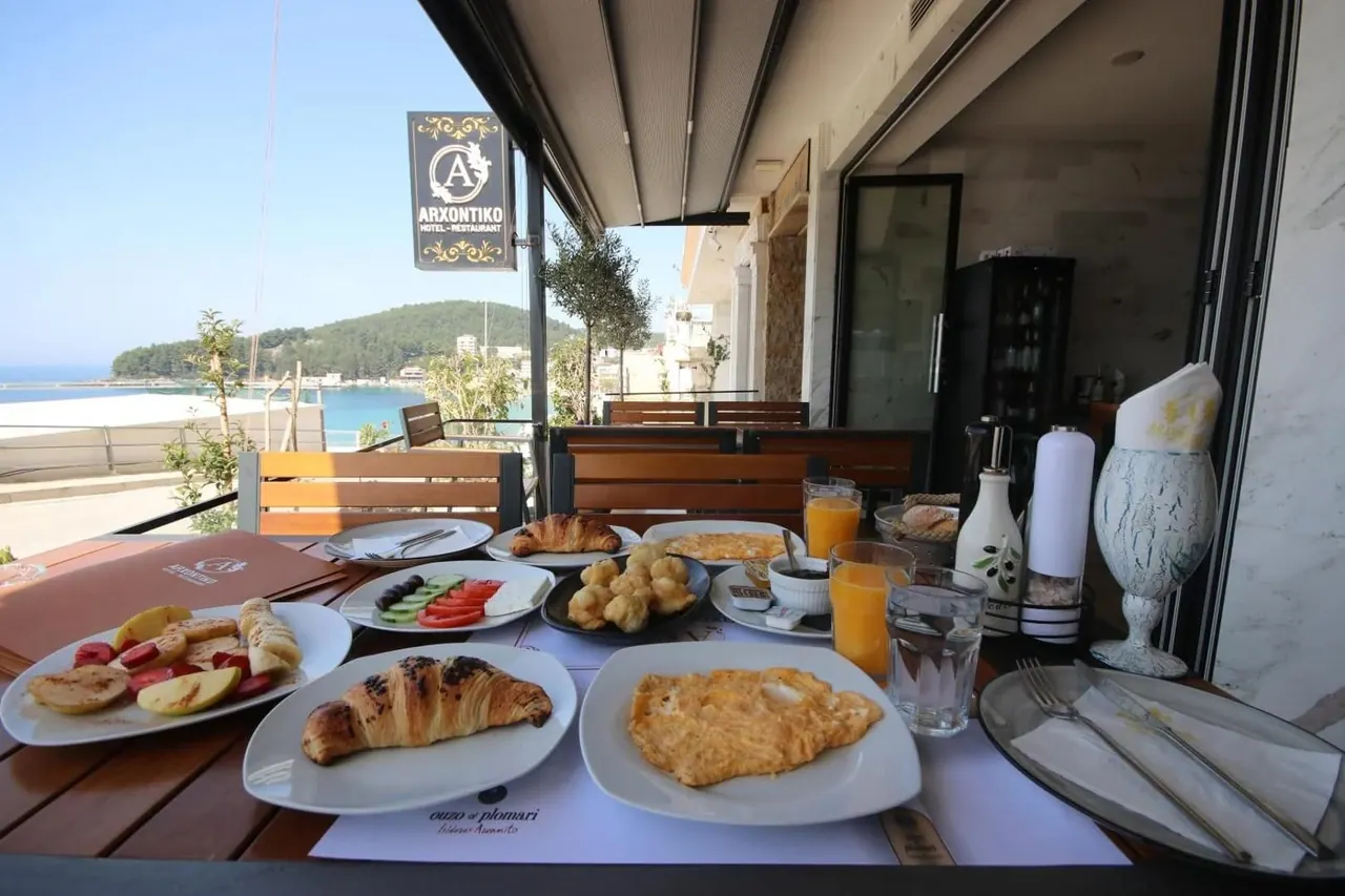 The Arxontiko Hotel-Restaurant sign hanging over a breakfast table on the terrace, with Spile bay behind it