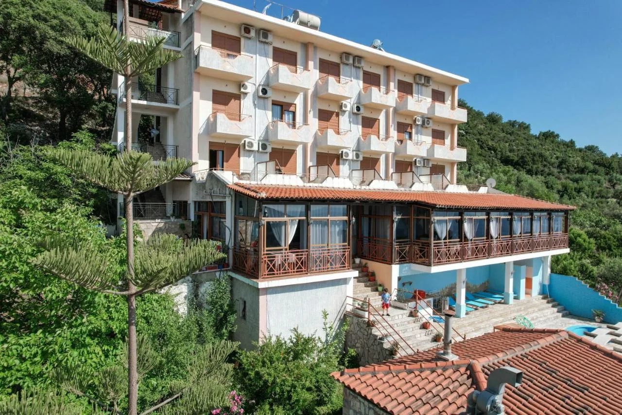 Hotel Panorama seen from one side, the block above its glazed veranda, the wooded hillside rising behind it, the pool and its paving to the right and the pantile roof of a lower outbuilding across the foreground.