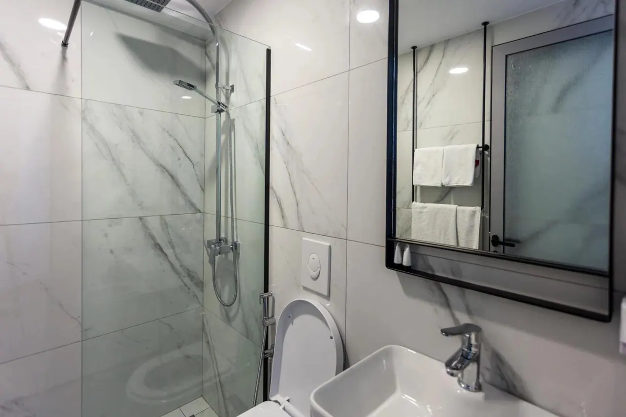 A marble-tiled bathroom with a glassed-in shower and folded towels on a rail