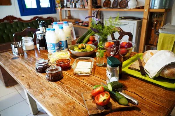 Breakfast laid out on the long wooden table at Himara Hostel: milk, jam, cheese, tomatoes, cucumbers and bread