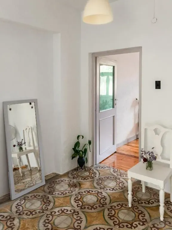Whitewashed hall at Himara Hostel with a leaning mirror, a white chair and a patterned encaustic cement tile floor