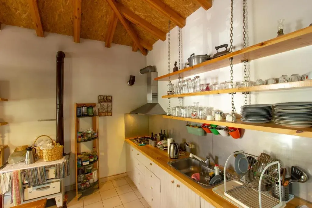 The shared kitchen at Himara Hostel: open timber shelves of glasses and plates hung on chains under a pitched wooden roof