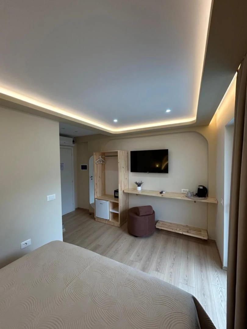 A room with a timber shelf and desk along the wall beneath a wall-mounted television, an arched niche beside it