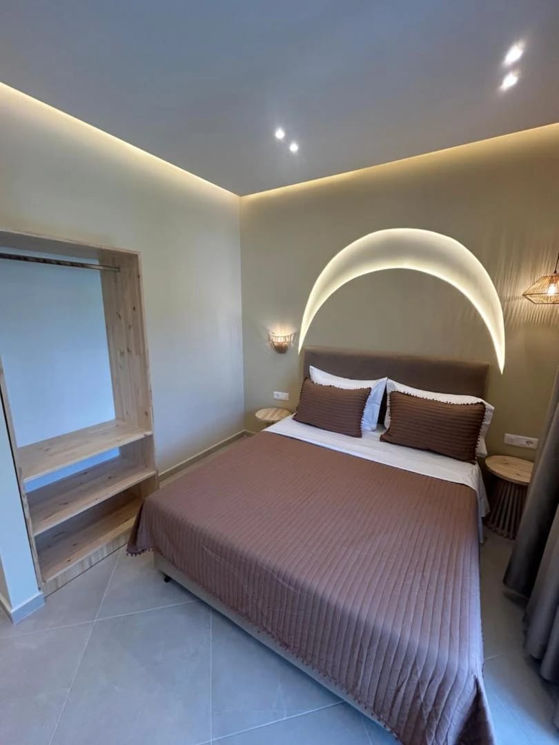 A double room with a domed arc of concealed light above the bed and an open timber wardrobe to the left
