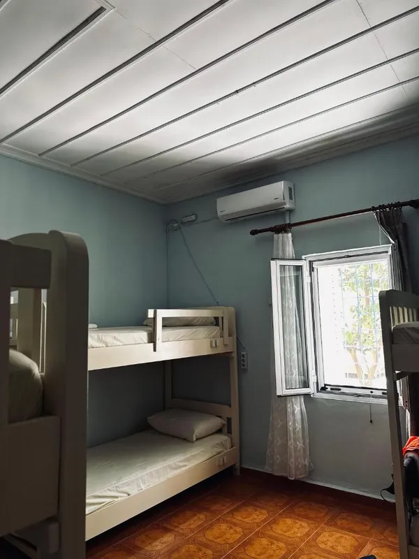 A dormitory with a bunk bed, an air-conditioning unit on the wall and an open window with a curtain