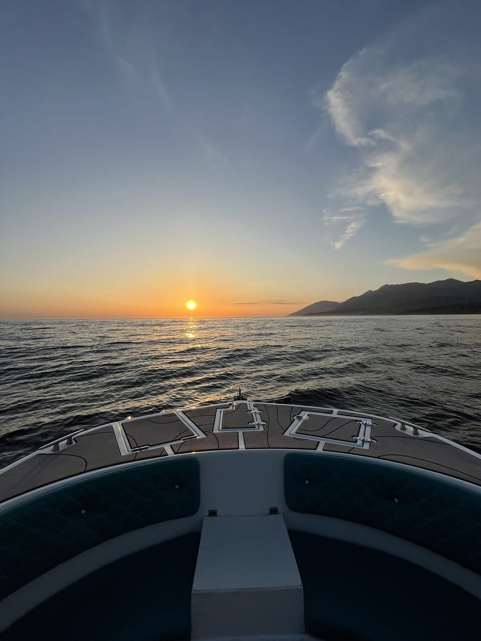 The sun setting into the Ionian seen over the bow of a boat off the Himarë coastline