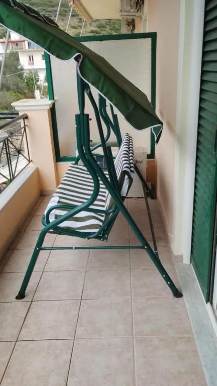A green canopied swing seat with striped cushions on a tiled balcony at Oasis Hostel