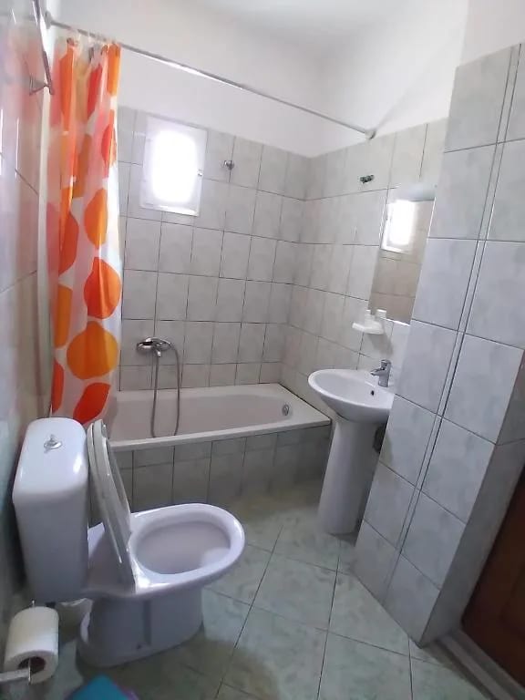 A tiled bathroom at Oasis Hostel with a bath, shower, basin and an orange patterned curtain