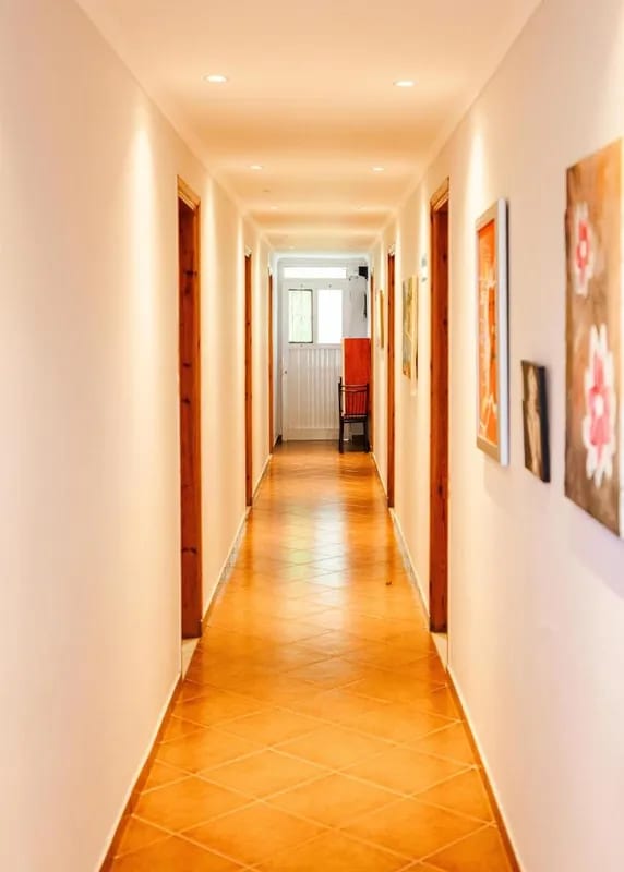 A lit corridor at Oasis Hostel with wooden doors, terracotta floor tiles and framed paintings