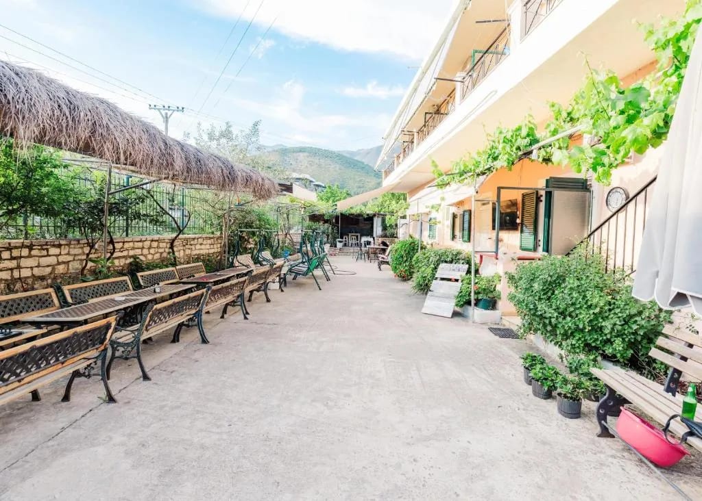The concrete yard at Oasis Hostel lined with wooden benches and potted plants, mountains behind