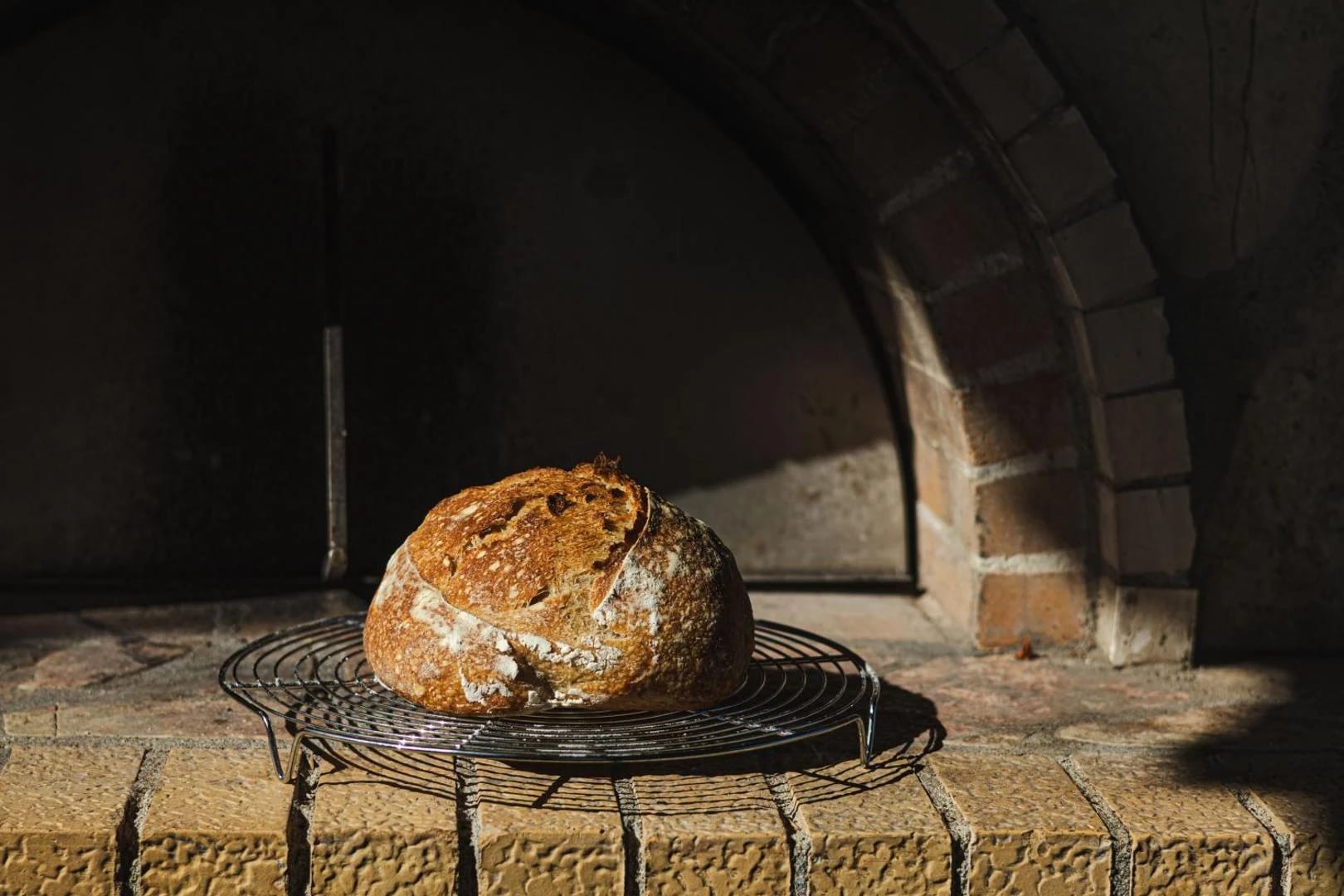 A round sourdough loaf cooling on a rack inside the mouth of the wood oven