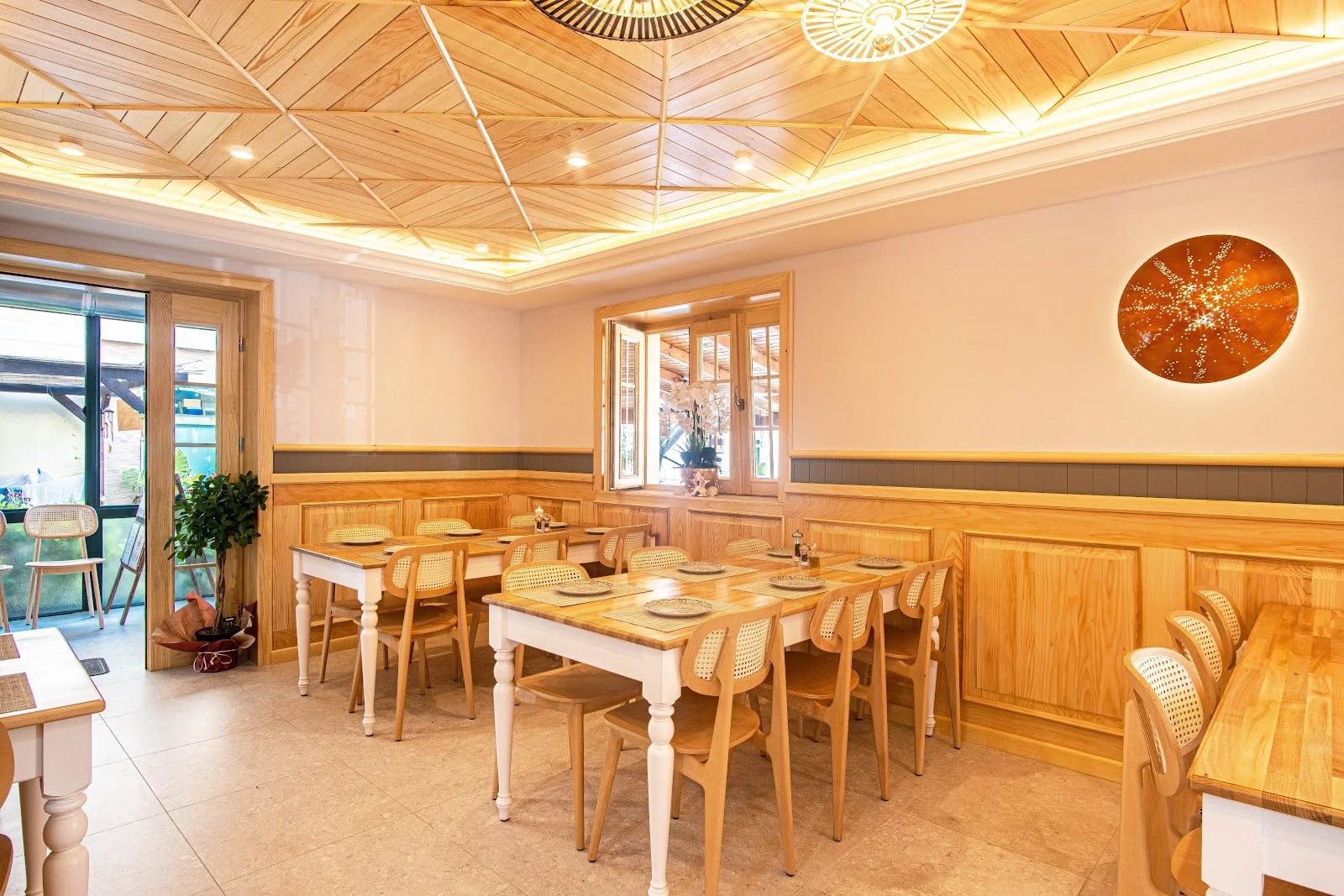 The dining room at Taverna Lefteri: pale ash panelling, a fitted timber ceiling, cane chairs and laid tables